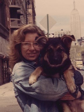 A photo of Kim Corcoran from the 1980s. She is standing on Broadway holding a puppy. The Empire State Building is visible behind her.